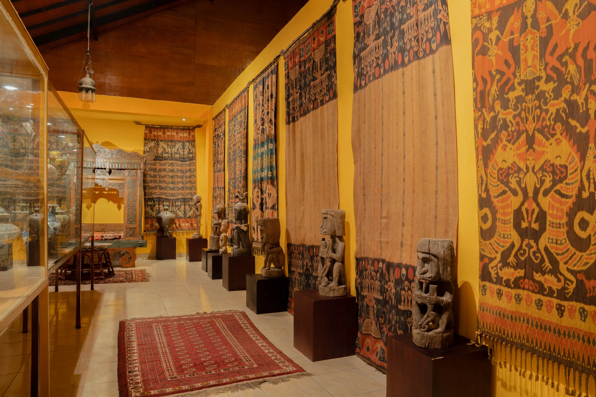 Wide view of the Ikat Room at Museum Peter Bloch Collection featuring traditional Balinese textiles and carved wooden structures.